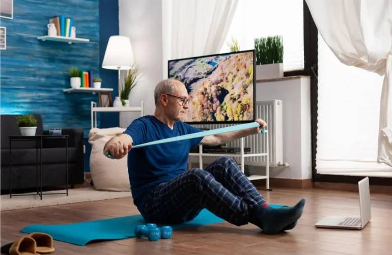 pensioner working body resistance exercising arms muscles using elastic band sitting yoga mat with crossed legs position senior man doing workout f 770x500 2