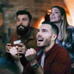 compressed young man cheering his team while watching sports championship with friends
