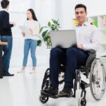 disabled smiling young businessman sitting wheelchair with laptop front business colleague 1