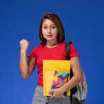 front view young female student red shirt wearing backpack holding files copybook rejoicing blue background 2