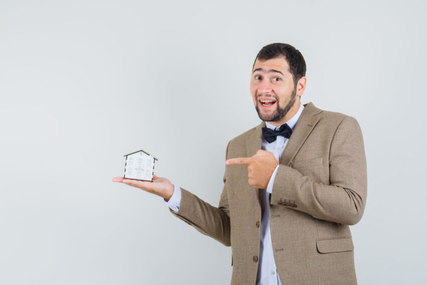 young male pointing house model suit looking cheerful front view optimized 1000