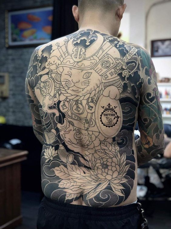 tattoo hình xăm mèo thần tài kín lưng đơn sắc Người đàn ông quay lưng, trên lưng có hình xăm lớn với hình mèo và các họa tiết phức tạp.
