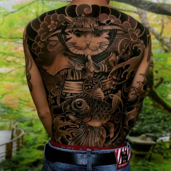 kín lưng xăm hình mèo nhẫn giả và cá chép Hình xăm lớn trên lưng với họa tiết mèo và cá chép, mang phong cách nghệ thuật truyền thống, nền thiên nhiên xanh.