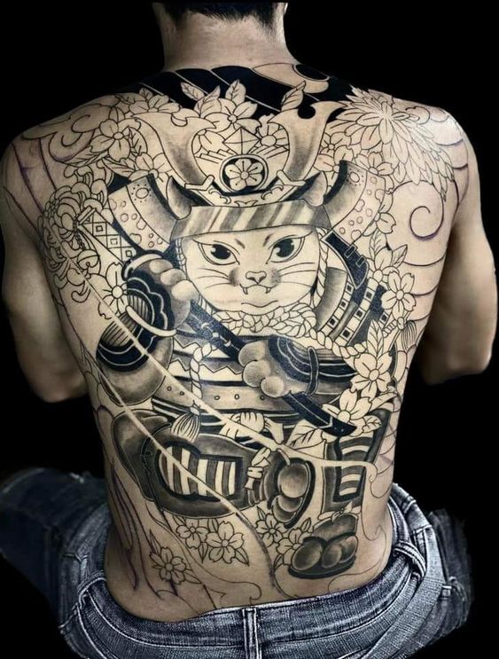 full lưng với hình xăm mèo thần tài samurai đơn sắc hoàn thiện Hình xăm lớn trên lưng người, mô tả một chiến binh mèo mặc giáp, xung quanh là hoa và họa tiết trang trí.