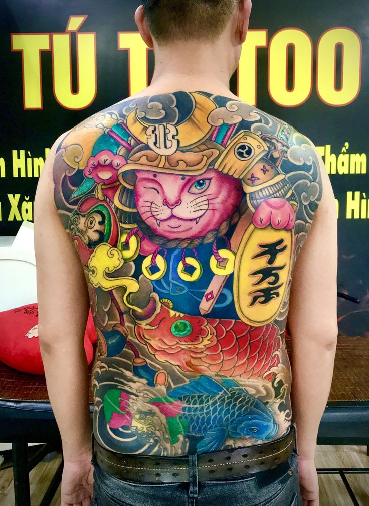 Hình xăm mèo thần tài samurai với nhiều họa tiết kiểu Nhật kín lưng Người với hình xăm lớn và nhiều màu sắc trên lưng, bao gồm mèo và cá chép, đứng trước biển quảng cáo.