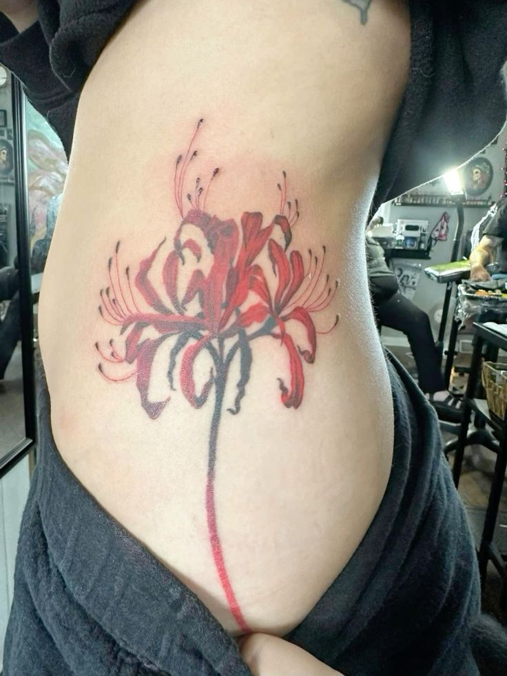H&igrave;nh xăm hoa m&agrave;u đỏ tr&ecirc;n v&ugrave;ng lưng của một người trong tiệm xăm nghệ thuật.