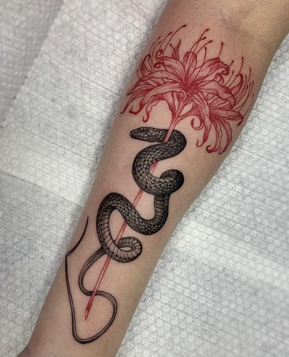 H&igrave;nh xăm tr&ecirc;n tay với h&igrave;nh rắn đen quấn quanh b&ocirc;ng hoa đỏ, nền vải trắng.