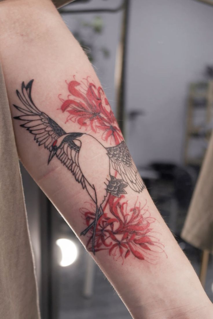 H&igrave;nh xăm tr&ecirc;n c&aacute;nh tay với h&igrave;nh chim v&agrave; hoa m&agrave;u đỏ, nền mờ.