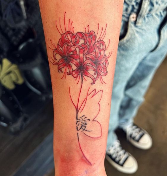 H&igrave;nh xăm hoa m&agrave;u đỏ tr&ecirc;n c&aacute;nh tay, c&oacute; chữ H&aacute;n ở th&acirc;n hoa, nền l&agrave; quần jeans v&agrave; gi&agrave;y thể thao.