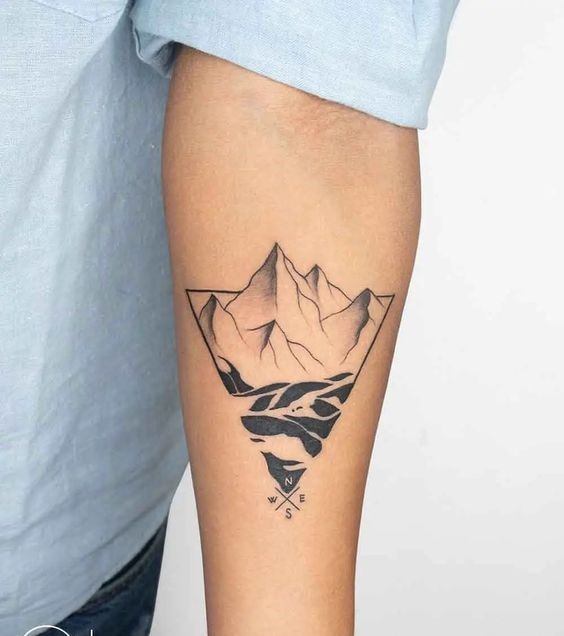 H&igrave;nh xăm tr&ecirc;n c&aacute;nh tay với thiết kế n&uacute;i v&agrave; la b&agrave;n độc đ&aacute;o, &aacute;o sơ mi xanh nhạt.