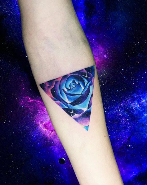 H&igrave;nh xăm hoa hồng xanh trong tam gi&aacute;c tr&ecirc;n c&aacute;nh tay, nền vũ trụ m&agrave;u t&iacute;m xanh rực rỡ.
