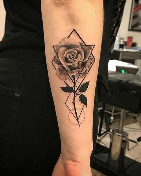 H&igrave;nh xăm hoa hồng v&agrave; h&igrave;nh học tr&ecirc;n c&aacute;nh tay, nền l&agrave; ph&ograve;ng xăm với ghế v&agrave; thiết bị.