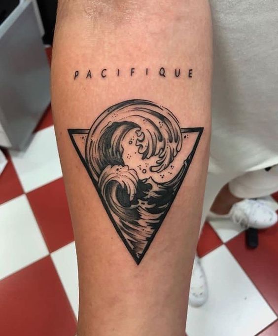 H&igrave;nh xăm tr&ecirc;n c&aacute;nh tay với s&oacute;ng biển trong h&igrave;nh tam gi&aacute;c v&agrave; chữ "PACIFIQUE" ph&iacute;a tr&ecirc;n.