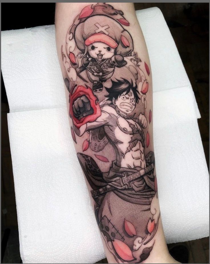 one piece đang chuẩn bị chiến đấu Hình xăm trên cánh tay với hai nhân vật hoạt hình, một người và một nhân vật nhỏ đội mũ, với các chi tiết màu đỏ.