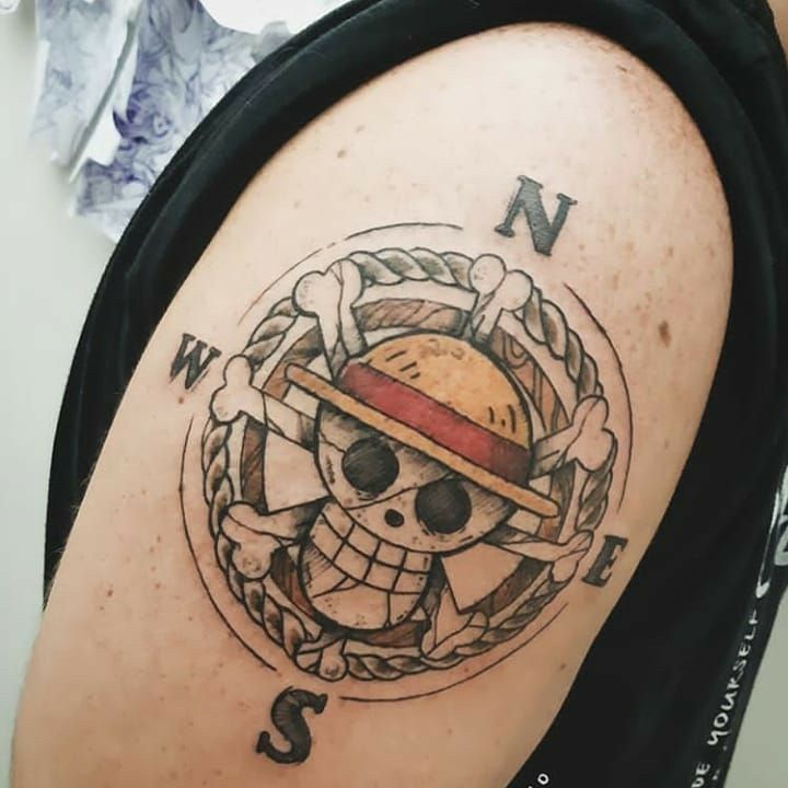 xăm one piece bốn phía Hình xăm trên cánh tay với biểu tượng đầu lâu đội mũ rộng vành, có các chữ cái chỉ hướng xung quanh.