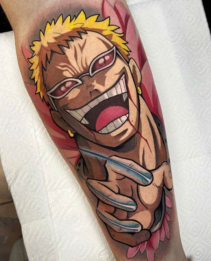 hình xăm one piece ngầu Hình xăm trên cánh tay, mô tả nhân vật hoạt hình với tóc vàng, kính râm và nụ cười lớn, có nền màu đỏ.