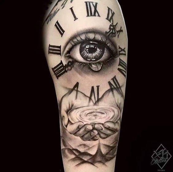 Hình xăm trên cánh tay với hình ảnh con mắt và đồng hồ số La Mã, bên dưới là đôi tay ôm lấy mặt nước.