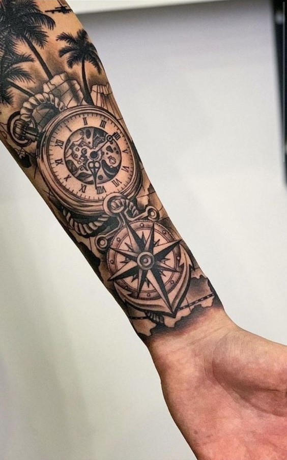 Hình xăm trên cánh tay với hình ảnh la bàn và đồng hồ cổ điển, xung quanh có cây cọ.