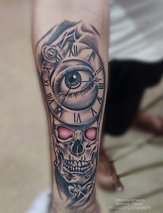 Hình xăm trên cánh tay với thiết kế gồm đồng hồ, con mắt và đầu lâu, sắc tố đen trắng.