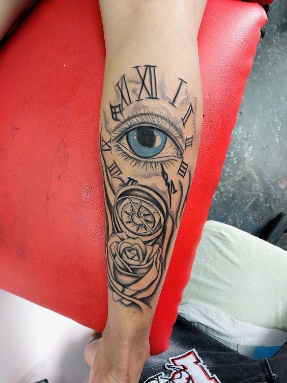 Hình xăm trên cánh tay gồm mắt, la bàn, hoa hồng và số La Mã, thiết kế trên nền ghế màu đỏ.