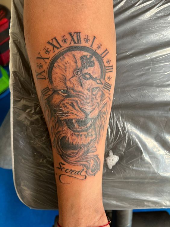 Hình xăm trên cánh tay với hình đầu sư tử và đồng hồ La Mã, có chữ "Secret" bên dưới.