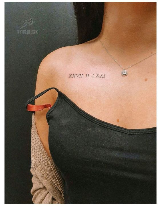 Hình xăm chữ số La Mã trên vai người đeo dây chuyền, mặc áo hai dây và áo khoác len.