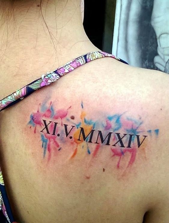 Hình xăm số La Mã trên vai với nền màu sắc pha trộn xanh, hồng và vàng.