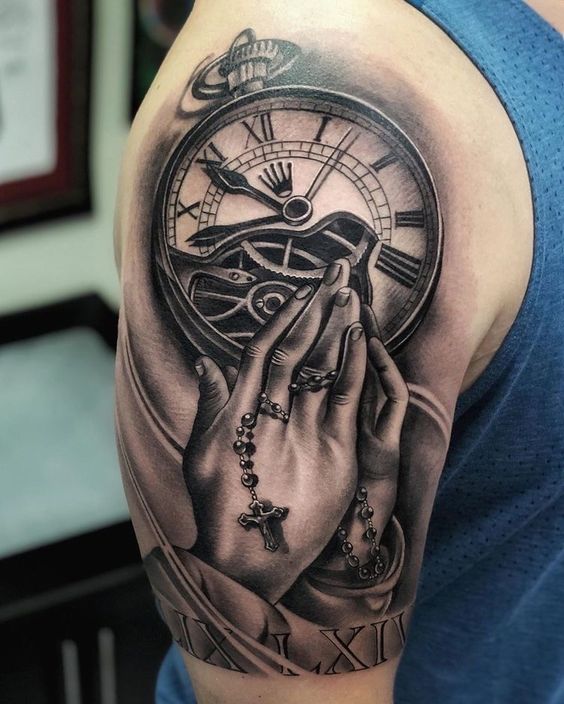 Hình xăm trên cánh tay với hình ảnh đồng hồ, bàn tay cầm chuỗi hạt và số La Mã, chi tiết rõ nét.