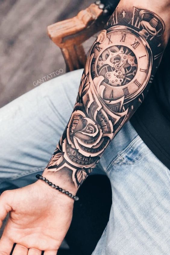 Cánh tay có hình xăm đồng hồ và hoa hồng, với chi tiết phức tạp, người mặc quần jean xanh nhạt.