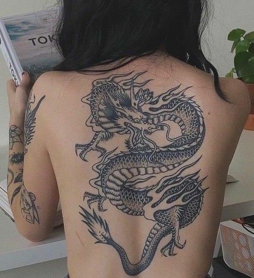 761c9609c5b7f27002fb974fb5834a78 Người quay lưng với hình xăm rồng lớn trên lưng, tay cầm quyển sách, ngồi cạnh chậu cây.
