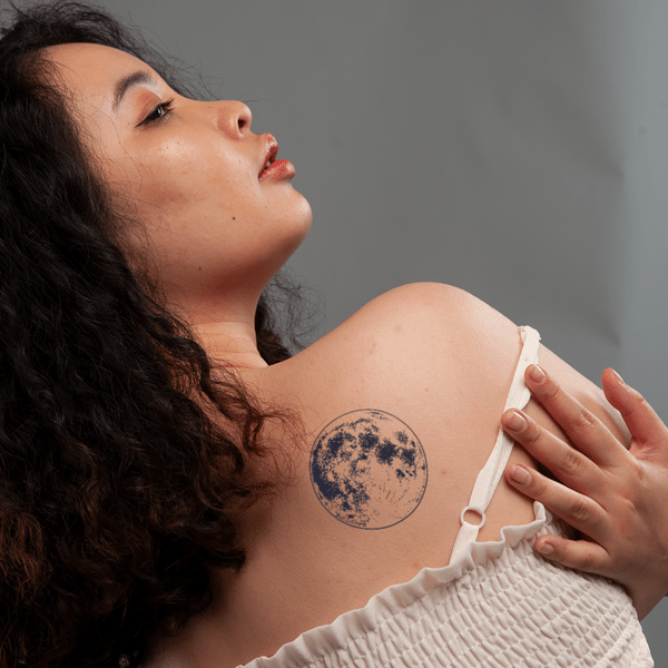 1_2__17__61af5e09f62844b1a641b8f3ac88d2d6_grande Người phụ nữ nhìn nghiêng, áp tay lên vai, có hình xăm tròn trên vai.