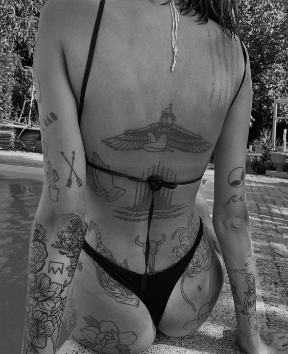 bcc490cb910dab14a0cd5b4f0b512e75 Người mặc bikini ngồi bên hồ bơi, lưng có nhiều hình xăm nghệ thuật, ảnh chụp đen trắng.