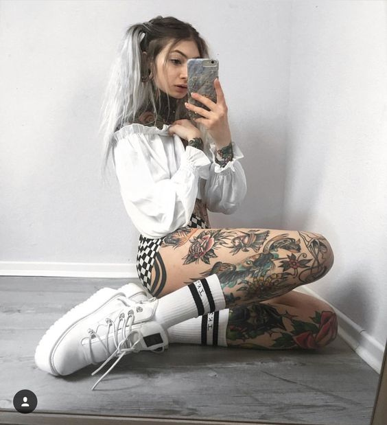 1bae24eb456bdbeb621036d5f2f35a82 Người chụp ảnh selfie trước gương, mặc áo trắng, quần sọc, giày trắng, và có nhiều hình xăm trên cơ thể.