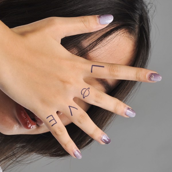 Người giơ tay với chữ "LOVE" tr&ecirc;n ng&oacute;n tay, m&oacute;ng tay sơn m&agrave;u t&iacute;m nhạt, nền x&aacute;m.