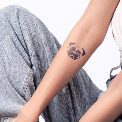 C&aacute;nh tay với h&igrave;nh xăm ch&oacute; pug, người mặc quần jeans xanh nhạt v&agrave; &aacute;o trắng.