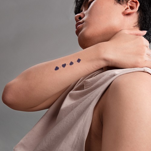 Người mặc &aacute;o kh&ocirc;ng tay chạm v&agrave;o cổ, tr&ecirc;n tay c&oacute; h&igrave;nh xăm bốn chất b&agrave;i t&acirc;y: cơ, r&ocirc;, chuồn, b&iacute;ch.