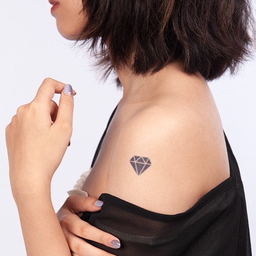 Người với t&oacute;c ngắn, h&igrave;nh xăm vi&ecirc;n kim cương tr&ecirc;n vai, mặc &aacute;o đen, tay chạm nhẹ v&agrave;o cổ &aacute;o.