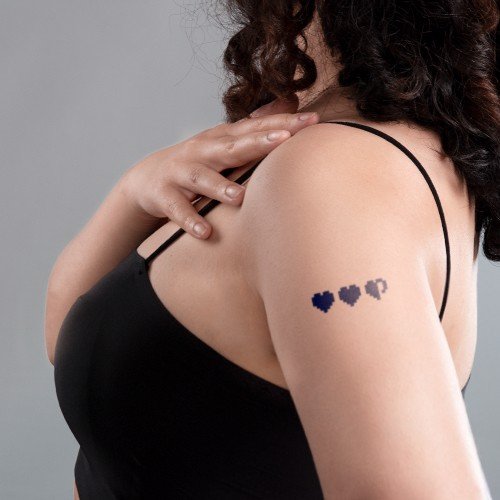 Người mặc &aacute;o đen, tay đặt tr&ecirc;n vai, c&oacute; h&igrave;nh xăm ba tr&aacute;i tim tr&ecirc;n c&aacute;nh tay.