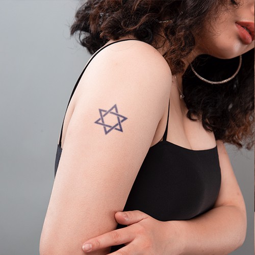 Người đeo hoa tai lớn đứng nghi&ecirc;ng, tr&ecirc;n c&aacute;nh tay c&oacute; h&igrave;nh xăm ng&ocirc;i sao s&aacute;u c&aacute;nh.