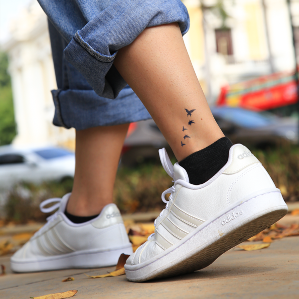 Một người đi gi&agrave;y thể thao trắng, quần b&ograve; xắn gấu, c&oacute; h&igrave;nh xăm chim tr&ecirc;n mắt c&aacute; ch&acirc;n.