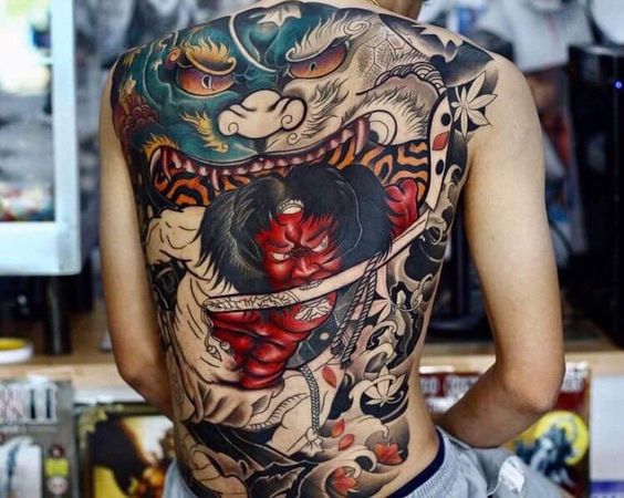 533ca4391c6696a04efe7c980207b0f4 Hình xăm lớn đầy màu sắc trên lưng một người, với hình ảnh mặt quỷ và họa tiết nghệ thuật truyền thống.