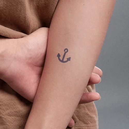 Cánh tay với hình xăm mỏ neo nhỏ, tay khác chạm nhẹ vào.