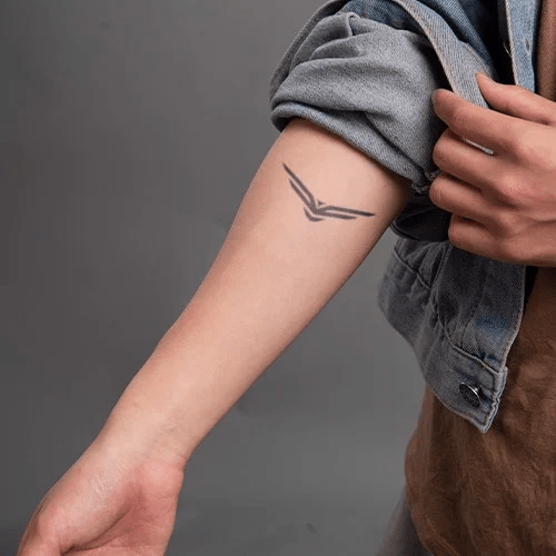 Cánh tay người với hình xăm thiết kế trừu tượng, tay áo cuộn lên, nền xám.