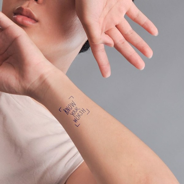 Người giơ tay, cánh tay có dòng chữ "KNOW YOUR WORTH", nền xám.