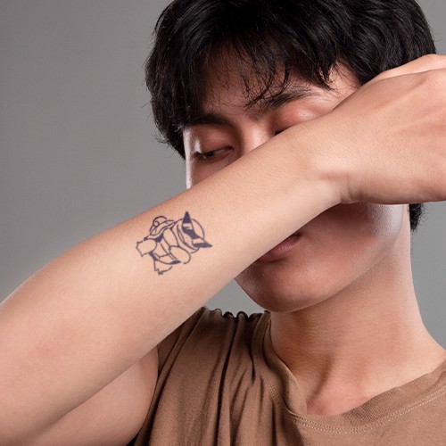 Người đàn ông che mặt bằng cánh tay, trên đó có hình xăm một con cáo cách điệu.