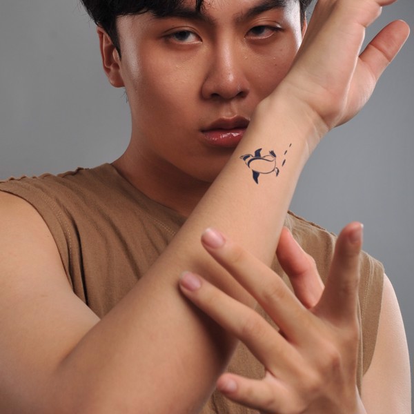 Người mặc áo không tay, tay giơ lên, có hình xăm cá heo trên cẳng tay, nền xám.