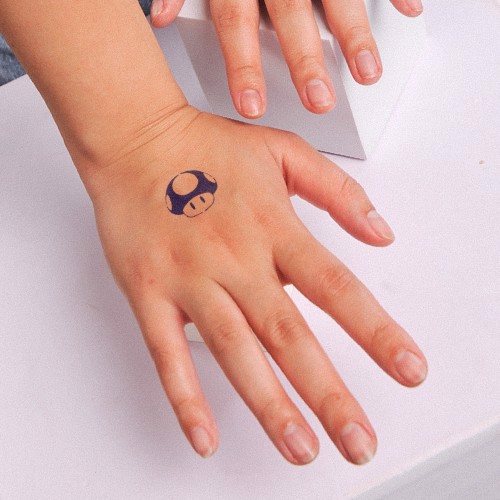 Một bàn tay với hình xăm tạm thời hình nấm trên mu bàn tay, đặt trên bề mặt màu trắng.