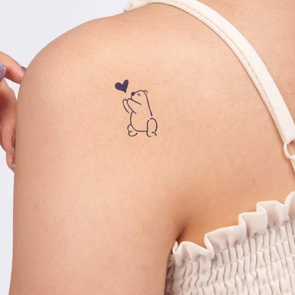 Hình xăm nhỏ trên vai một người, mô tả gấu và trái tim, người mặc áo dây màu sáng.