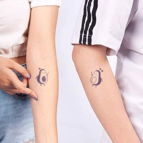 Hai cánh tay với hình xăm quả bơ dễ thương, một tay có trái tim bay quanh.