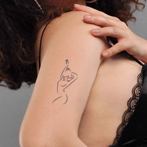 Một cánh tay với hình xăm nghệ thuật tối giản của một người đang giơ tay, nền xám và áo có ren đen.